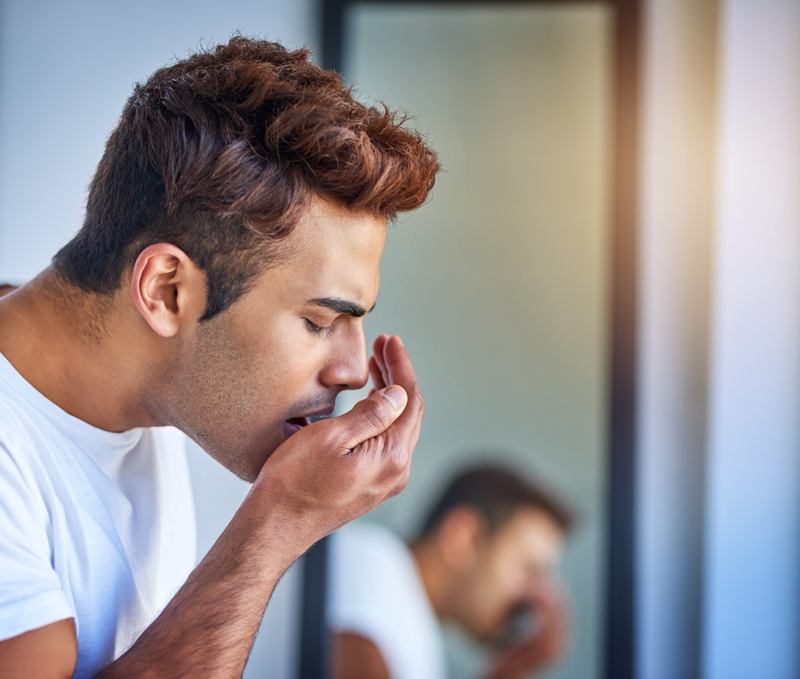 man blowing into his hand checking for bad breath, dental hygiene